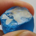 Blauer Topaskristall mit glatter, reflektierender Spaltfläche.