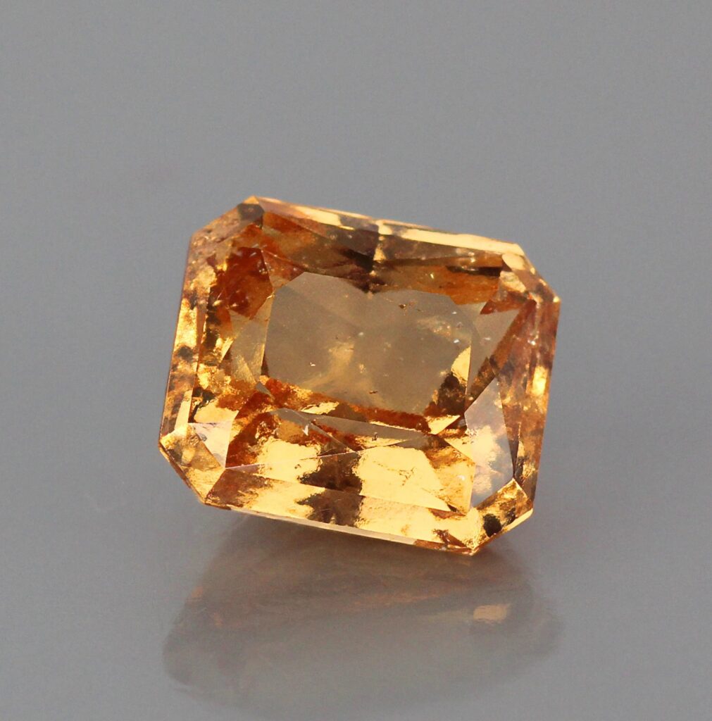 このエメラルドカットのヘソナイトは、カルシウムアルミニウムケイ酸塩の組成に特徴的な、鮮やかな蜂蜜色を帯びたオレンジ色と、はっきりとしたシナモンブラウンの基調色を呈している。