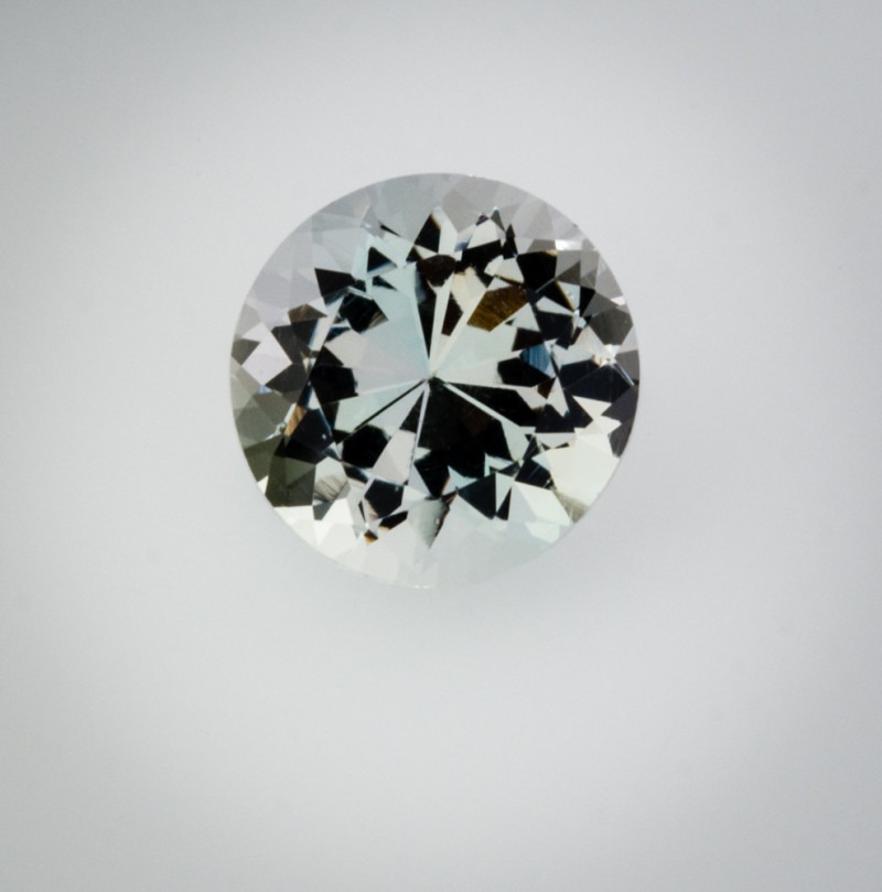 一颗刻面圆钻型切磨的无色奥长石宝石，展现出极高的玻璃光泽。在专业摄影棚光照下，其精确的几何刻面排列在对比鲜明的浅灰色背景下折射出迷人的光芒。