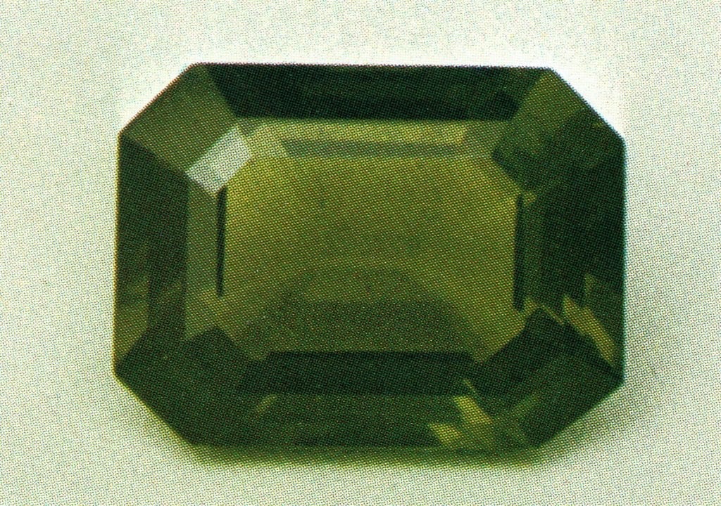 An emerald-cut faceted ekanite gemstone from Sri Lanka, displaying a characteristic deep olive green color and vitreous luster.