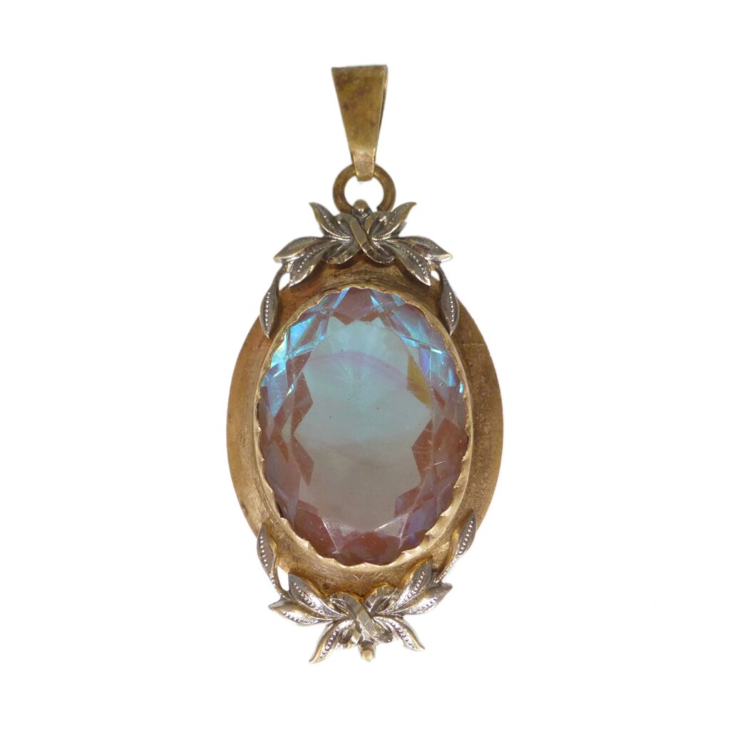 A vintage pendant featuring an oval faceted Saphiret glass stone set in a decorative gold-tone frame with leaf-like details, displaying characteristic blue and brown color shifts.