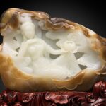 Eine kunstvolle chinesische Nephrit-Jade-Schnitzerei auf einem geschnitzten Holzständer. Die zentralen Figuren aus weißer Jade stellen Guanyin und einen Begleiter dar, umgeben von Wolken und einen Lotus haltend, alles eingeschlossen in eine natürliche braune und lohfarbene Nephrit-Rinde oder „Haut“-Schale vor einem schwarzen Verlaufshintergrund.