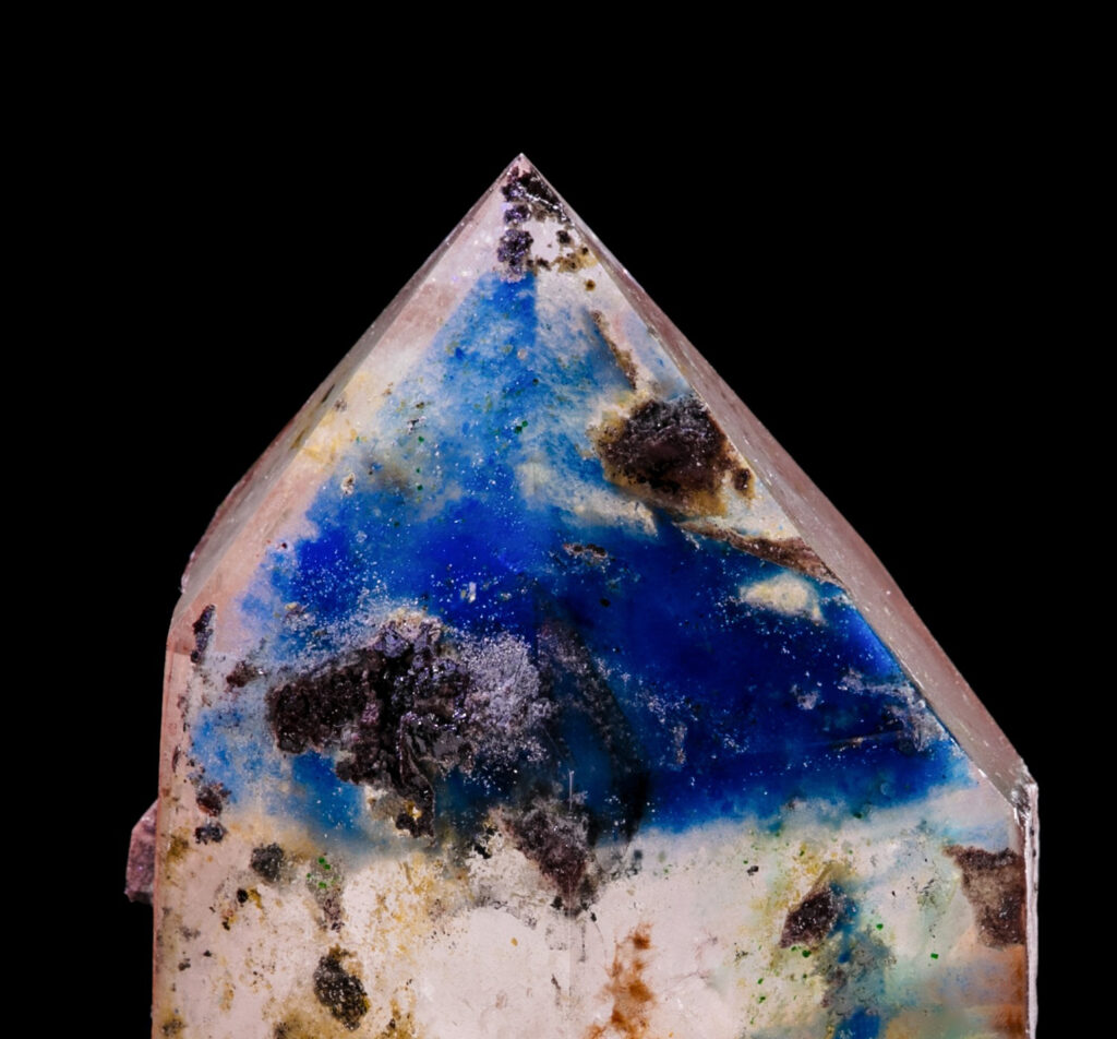 一粒透明石英晶尖的特写镜头,其内部呈现饱和的电蓝色帕帕戈石幻影包裹体,映衬在漆黑的背景之上。