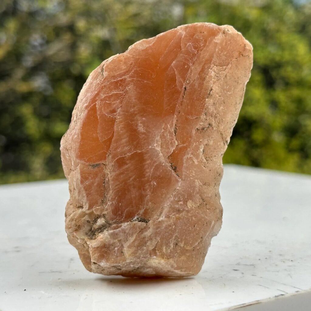 一张未经抛光的日长石（奥长石）原石标本特写，呈现出半透明的桃橙色。