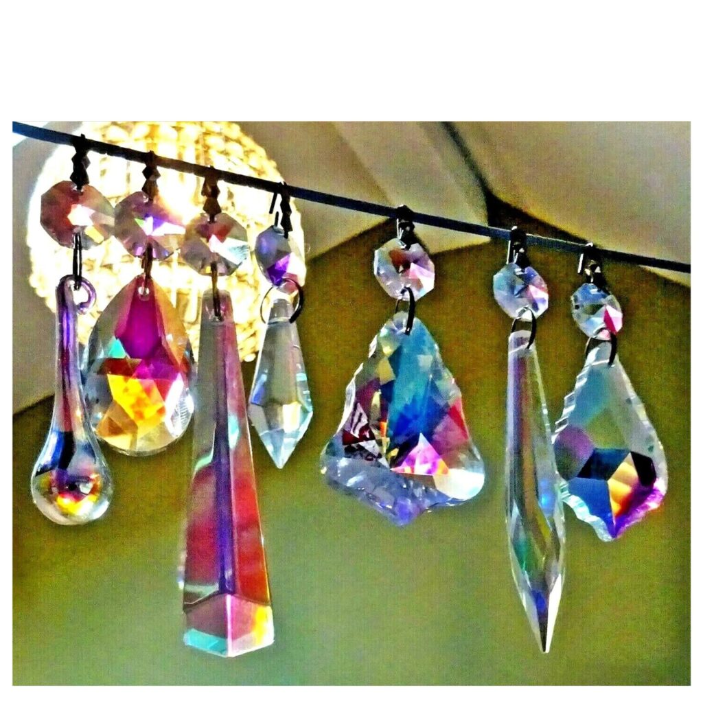 A collection of various faceted Aurora Borealis (AB) glass prisms hanging in a row, each exhibiting vibrant, rainbow-like iridescent flashes and reflections.