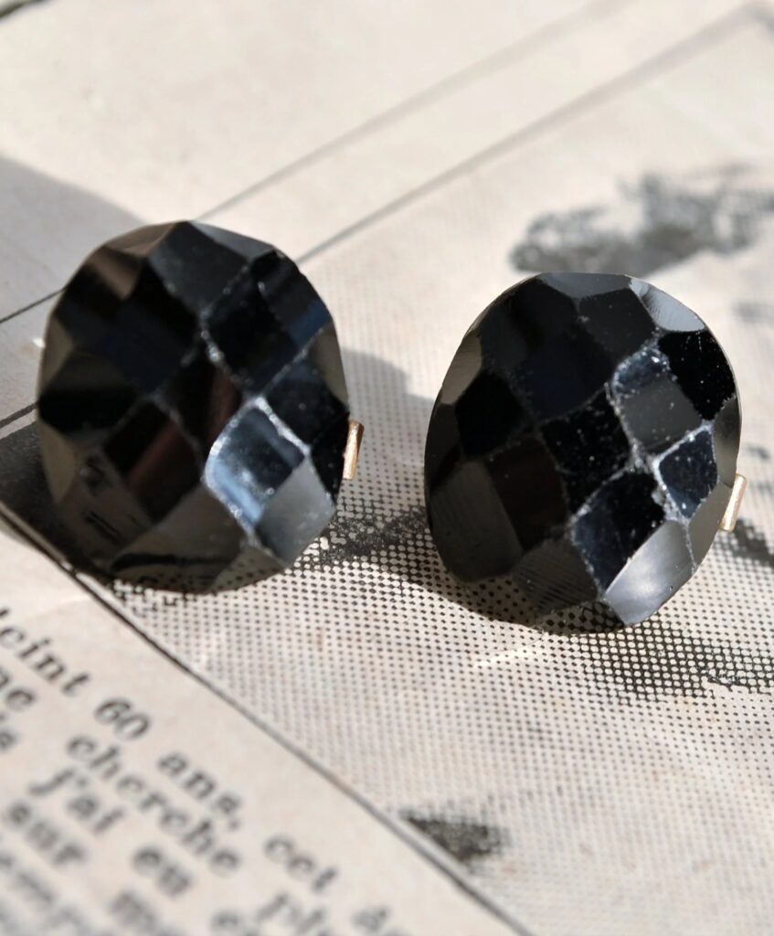 A pair of vintage faceted black glass cufflinks, historically known as French Jet, resting on a piece of old printed newspaper.