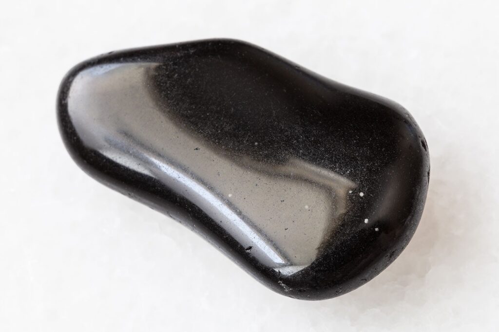 Tumbled, smooth, and glossy piece of man-made obsidian, also known as vulcan glass, exhibiting a deep, uniform black color and vitreous luster typical of this synthetic material.