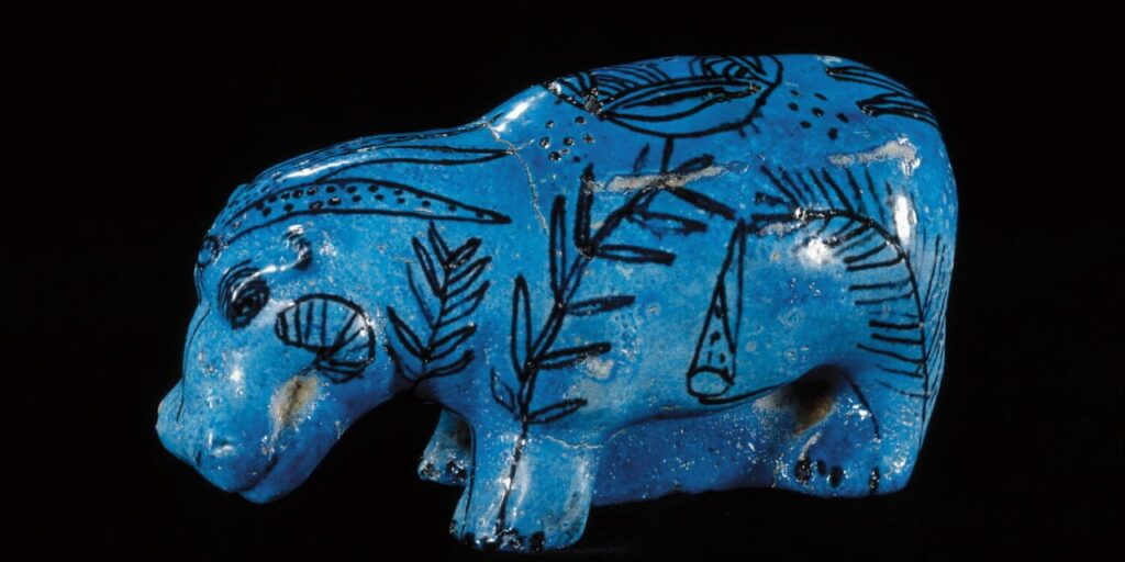 Vibrant blue Egyptian Faience figurine of a hippopotamus, decorated with intricate black line drawings of marsh plants and flowers, showcasing the classic glazed surface of ancient artifacts.