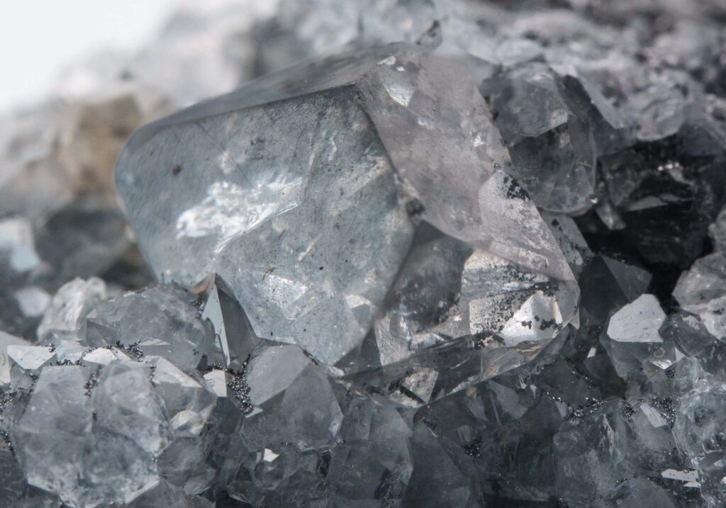 A detailed macro view of translucent Anglesite crystals containing dark, smoky grey inclusions. These "phantoms" are caused by microscopic particles of unoxidized galena trapped within the lead sulfate crystal lattice.