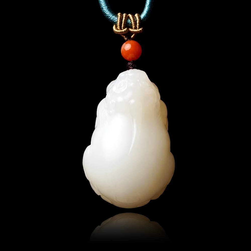 A high-quality white nephrite jade pendant carved in the shape of a mythical creature, featuring a smooth "mutton fat" texture, suspended by a blue silk cord with a decorative red bead.
