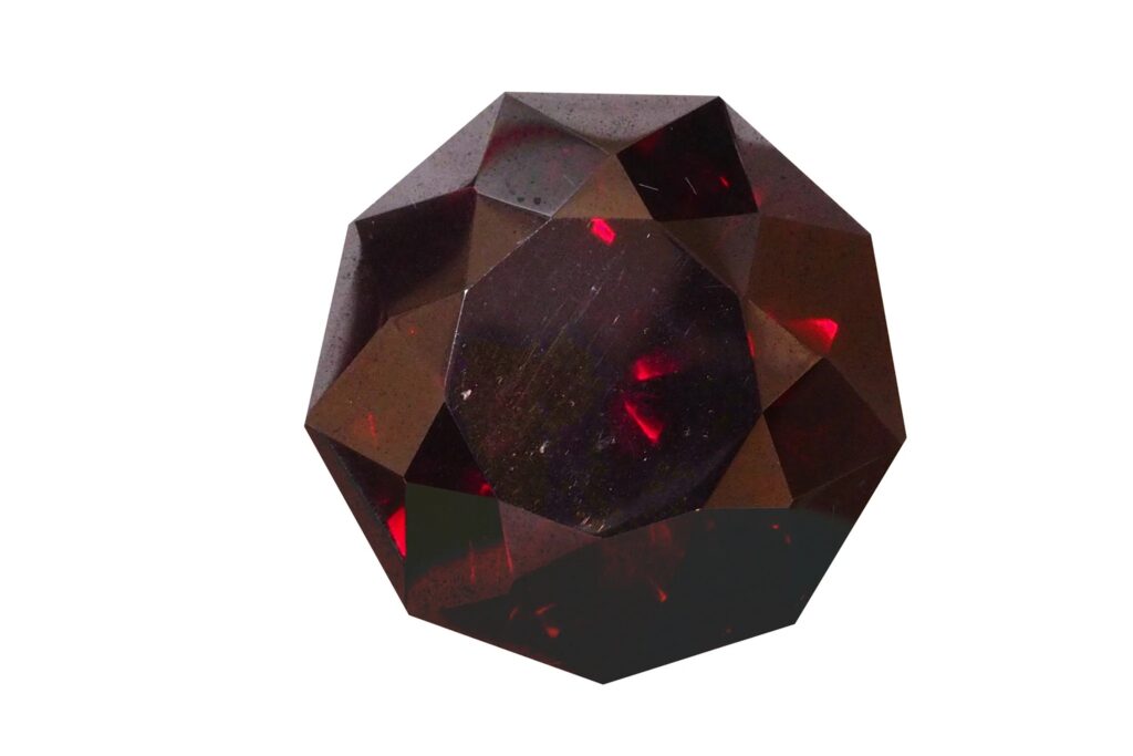 Ein facettierter, dunkelroter Cuprit-Kristall mit internem karmesinrotem Aufblitzen.