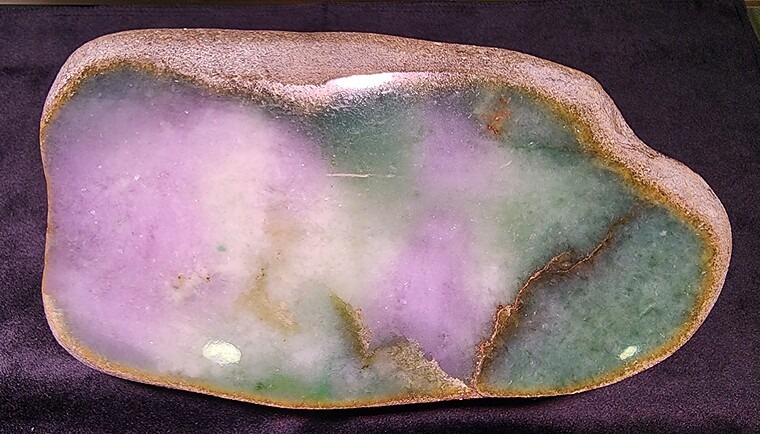 Polished slab of a jadeite jade boulder showing characteristic lavender and green mottling, with visible natural fractures and a weathered outer crust (rind), sourced from Myanmar.