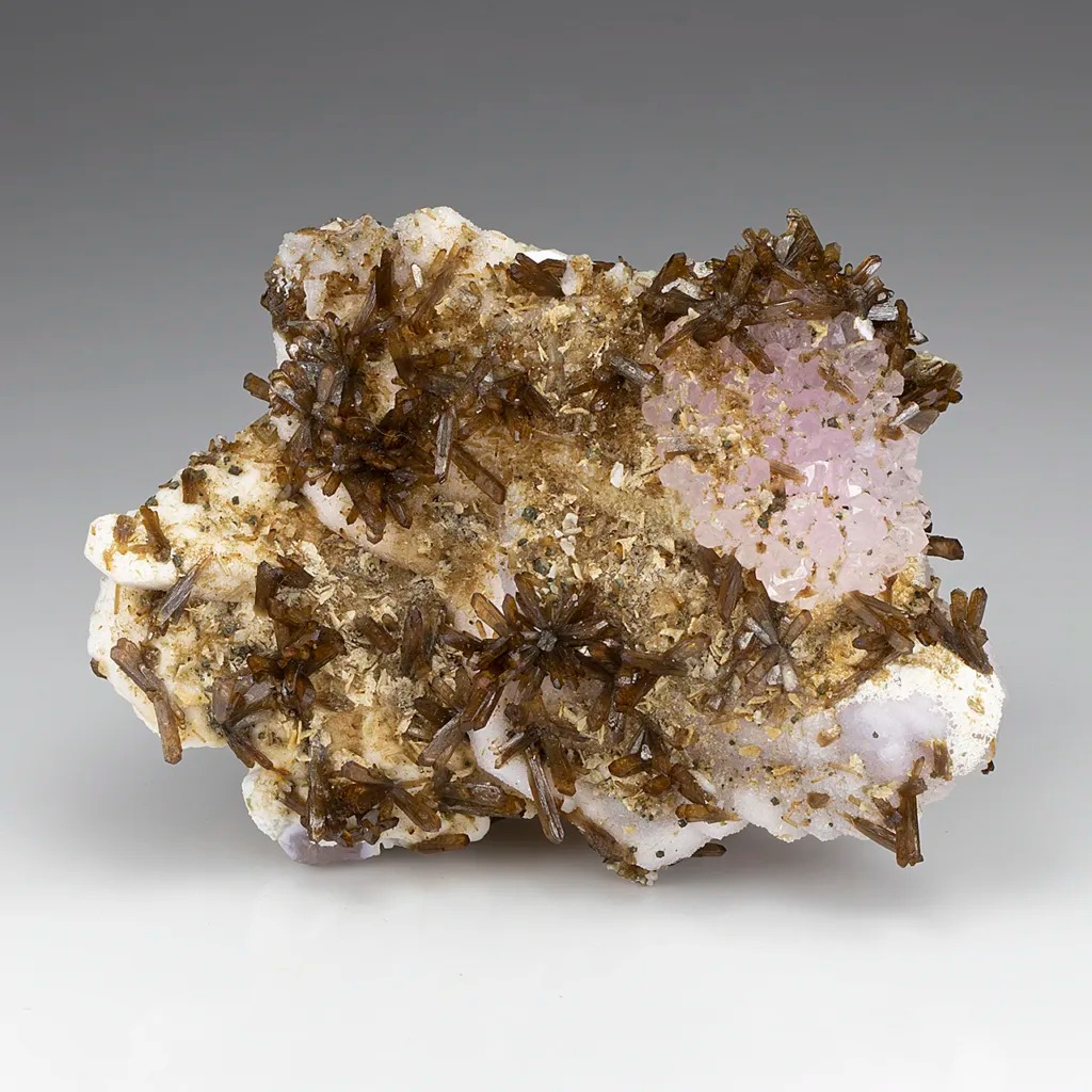 Amas radiants de cristaux d'éosphorite brunâtre sur une matrice minérale présentant un amas de quartz rose pâle.