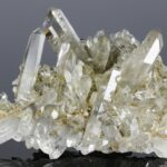 Eine Stufe aus transparenten, farblosen Quarzkristallen mit kleineren, milchweißen Adular-Kristallen an der Basis