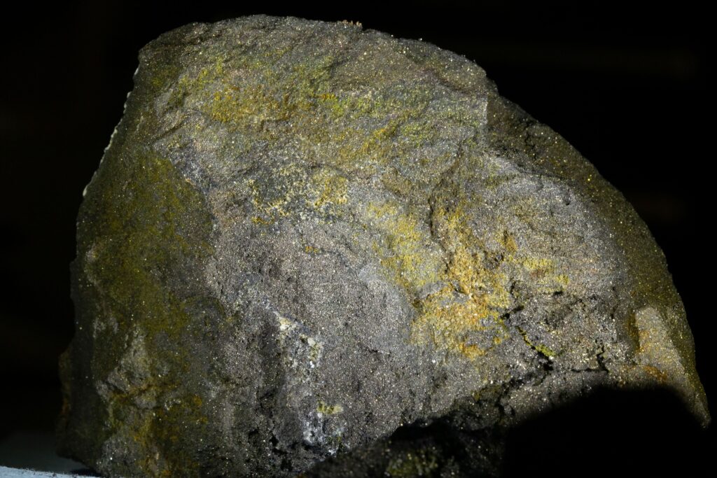 Eine massige, pyrrhotinreiche Sulfiderzprobe mit einer körnigen, metallisch bronzegelben Textur.