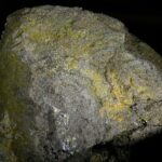 Eine massige, pyrrhotinreiche Sulfiderzprobe mit einer körnigen, metallisch bronzegelben Textur.
