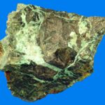 Niccolit-Mineralprobe mit sekundären grünen Annabergit-Oxidationskrusten und -adern auf einer metallischen Oberfläche.