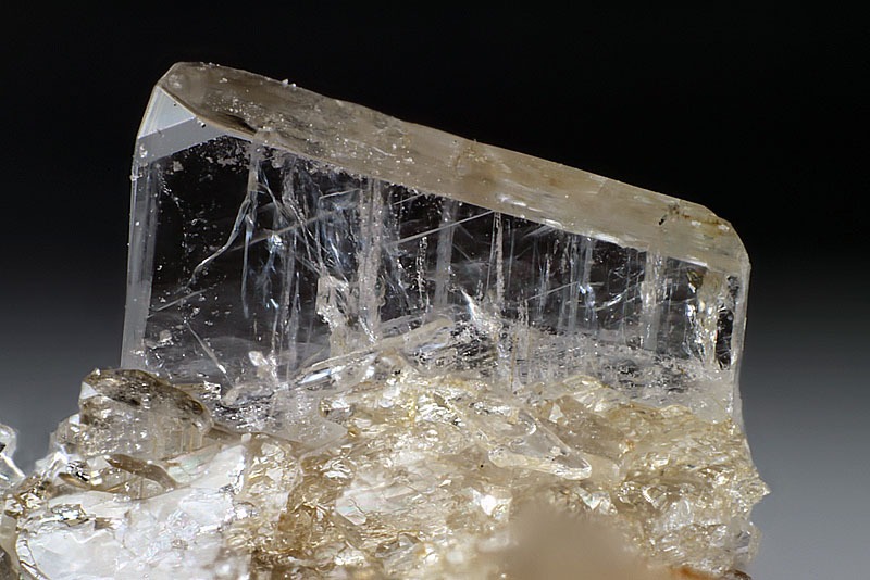 A transparent, tabular Sanidine crystal with a vitreous luster, showcasing its characteristic monoclinic structure and glassy clarity.