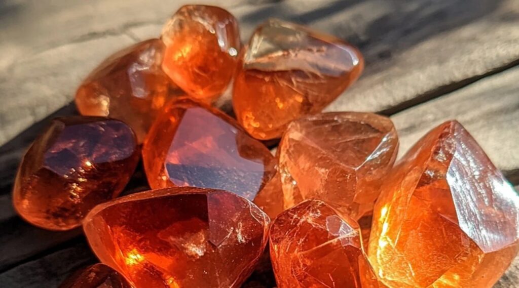 태양광 아래에서 천연 내포물과 유리 광택을 보여주는 연마된 오렌지 안데신 결정체 모음.