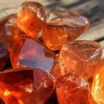 Eine Sammlung polierter oranger Andesin-Kristalle, die unter Sonnenlicht natürliche Einschlüsse und Glasglanz zeigen.