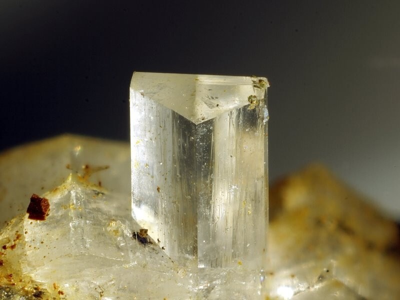 A clear, prismatic orthoclase crystal specimen showing a well-defined monoclinic structure on a rocky matrix.