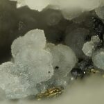 Nahaufnahme-Makrofotografie von durchscheinenden weißen Prosopit-Mineralproben, die charakteristische strahlige, botryoidale (traubenförmige) Kristallstrukturen auf einer dunklen Matrix zeigen.