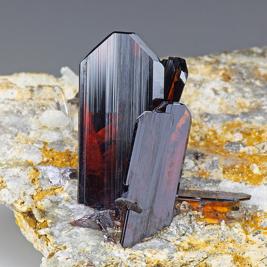 Deep red brookite crystals with vertical grooves on stone.