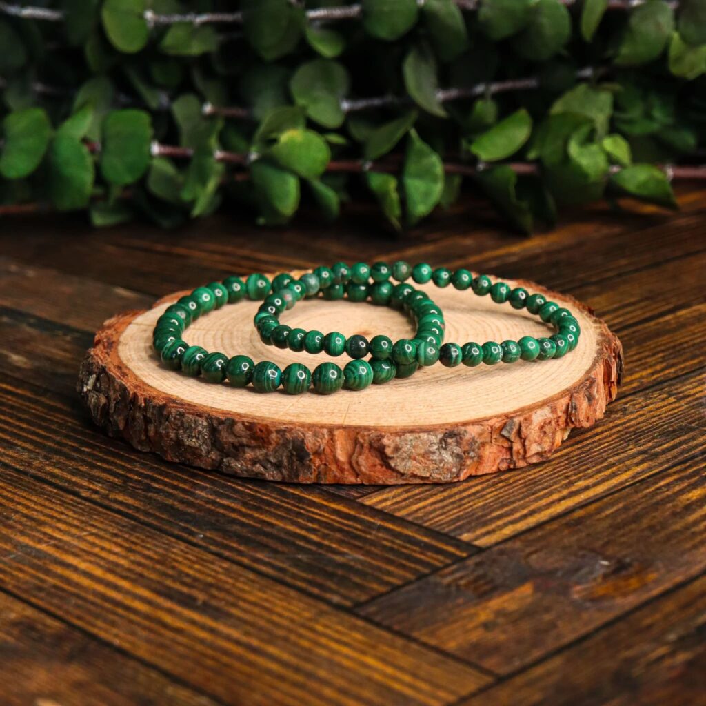 Two natural malachite beaded bracelets on a round wooden slice