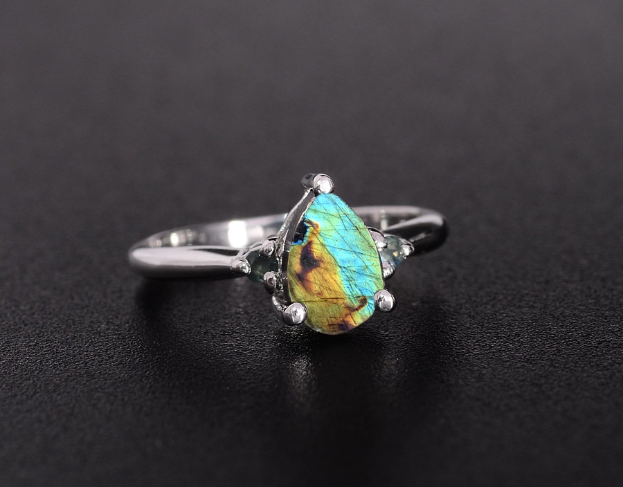 A silver ring featuring a pear-shaped Spectrolite gemstone with vibrant blue, green, and gold iridescence.
