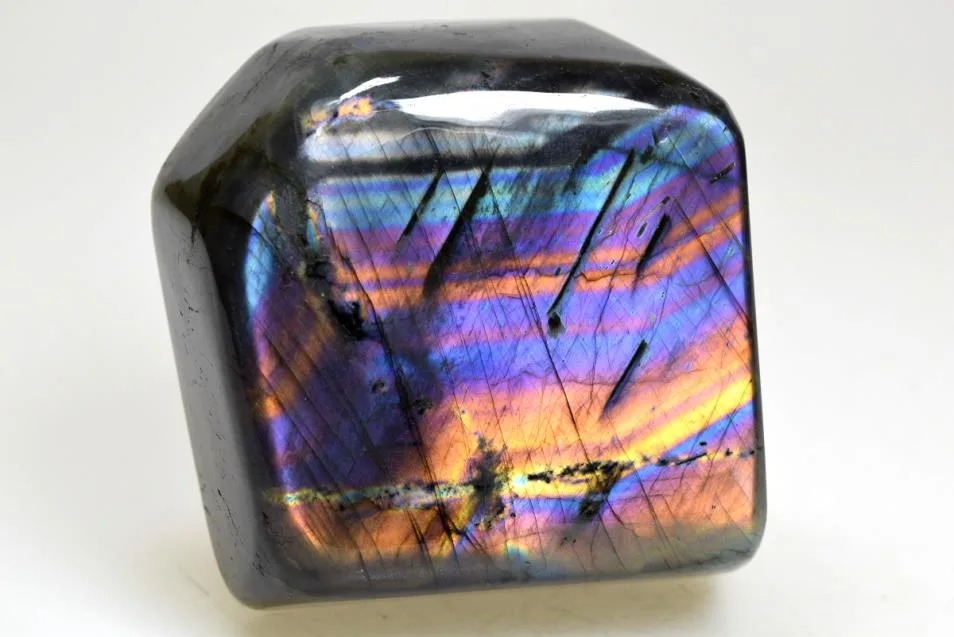 A polished Spectrolite gemstone displaying vibrant rainbow-colored iridescence on a dark base.