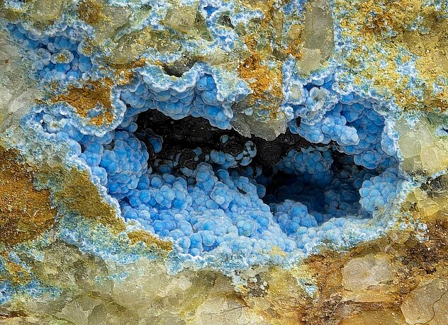 Natürliche Céruleit-Mineralienprobe mit leuchtend himmelblauen, botryoidalen oder traubenartigen Aggregaten, die sich in einem Gesteinshohlraum gebildet haben.