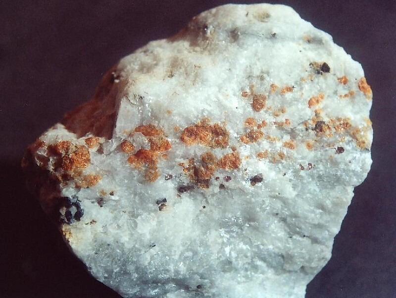 一块白大理岩标本，其上分布着橙褐色块硅镁石（Norbergite）晶体的散状颗粒集合体，并伴有少量的深色包裹体