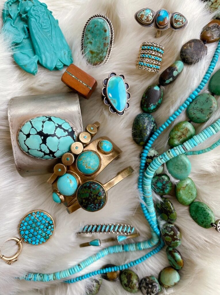 An assortment of turquoise jewelry, including rings, beaded necklaces, and wide cuff bracelets, displayed on a white fluffy surface.