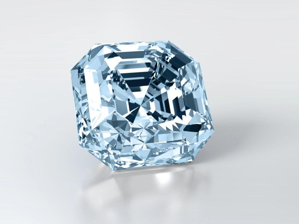 Ein loser, hellblauer Diamant in präzisem Asscher-Schliff, der symmetrische geometrische Facetten und brillante Reinheit aufweist und auf einer sauberen, reflektierenden weißen Oberfläche ruht.