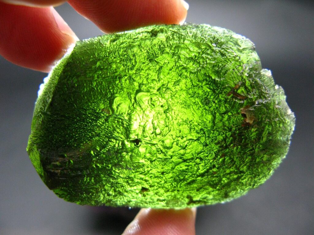 หินมอลดาไวต์ดิบสีเขียวที่ถืออยู่ระหว่างนิ้ว